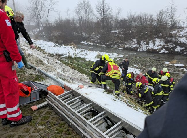Rettungskräfte arbeiten gemeinsam an einem Einsatz mit einer Leiter an einem schneebedeckten Ufer | © Name.