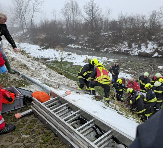 Rettungskräfte arbeiten gemeinsam an einem Einsatz mit einer Leiter an einem schneebedeckten Ufer | © Name.