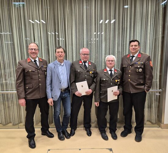 Fünf Männer in Uniform stehen mit Urkunden vor einem Vorhang, strahlend und stolz bei einer Auszeichnung | © Name
